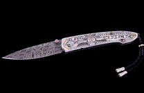 Custom folding knife with a patterned Damascus blade and an ornate silver handle featuring a stylized owl, geometric engravings, gold accents, and pink gems.