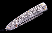 Silver-toned metal knife handle with intricate engraved eagle and geometric patterns, accented with gold and bronze, and a black cord.