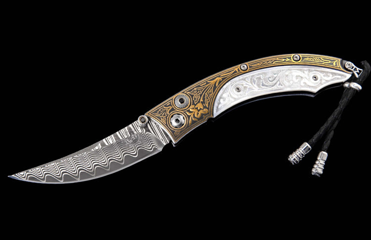 Ornate folding knife with a wavy Damascus steel blade and a handle featuring gold floral and white scroll engravings, with a black braided lanyard.