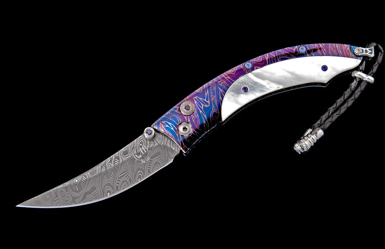Ornate folding knife with Damascus steel blade, iridescent purple handle, mother-of-pearl inlays, blue gemstone accents, and braided black lanyard.