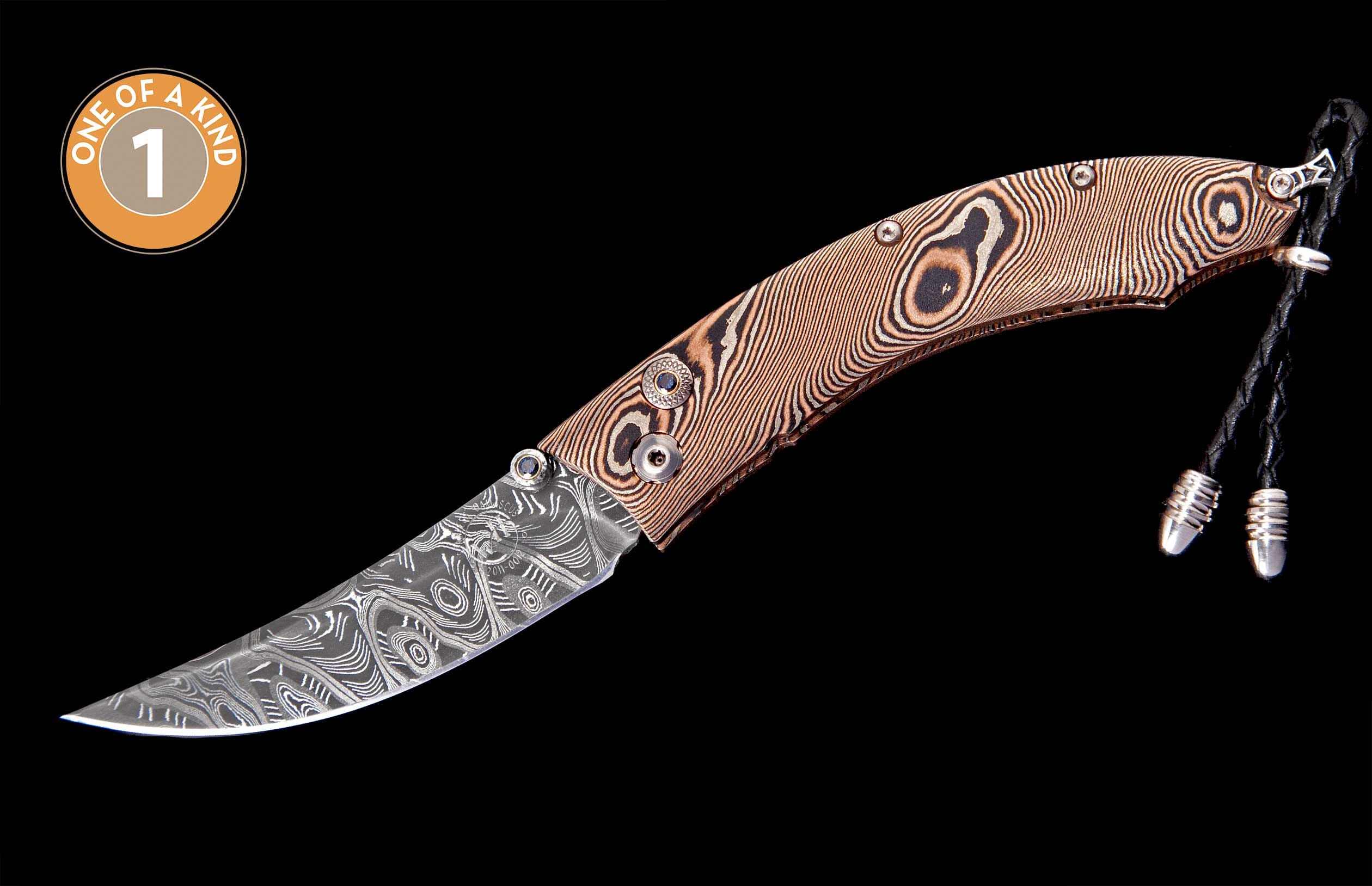 Ornate folding knife with patterned Damascus blade and copper-toned layered handle, featuring blue gemstones and a black braided lanyard.