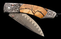 Folding knife with a light brown cracked handle, carved silver dragon bolsters with red gems, and a wavy Damascus steel blade.