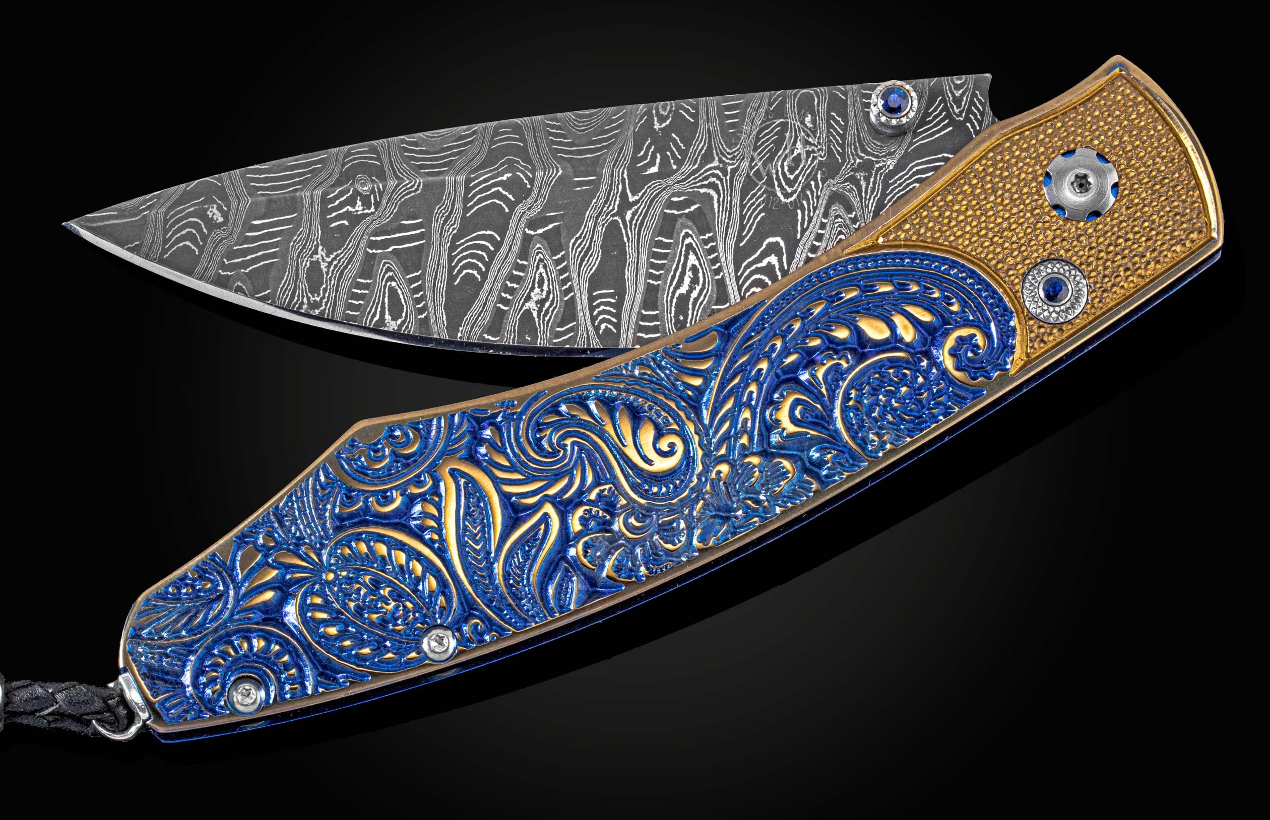 An open knife with an ornate blue and gold paisley handle and a wavy patterned Damascus steel blade.