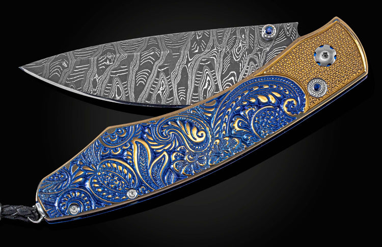 An open knife with an ornate blue and gold paisley handle and a wavy patterned Damascus steel blade.