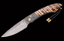 Elegant folding knife with a Damascene blade, brown striped handle, a dark patterned bolster, and a black braided lanyard with gold accents.