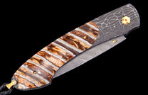 Folding knife with a striped brown and white handle, Damascus steel frame and blade, gold pins, and black lanyard.