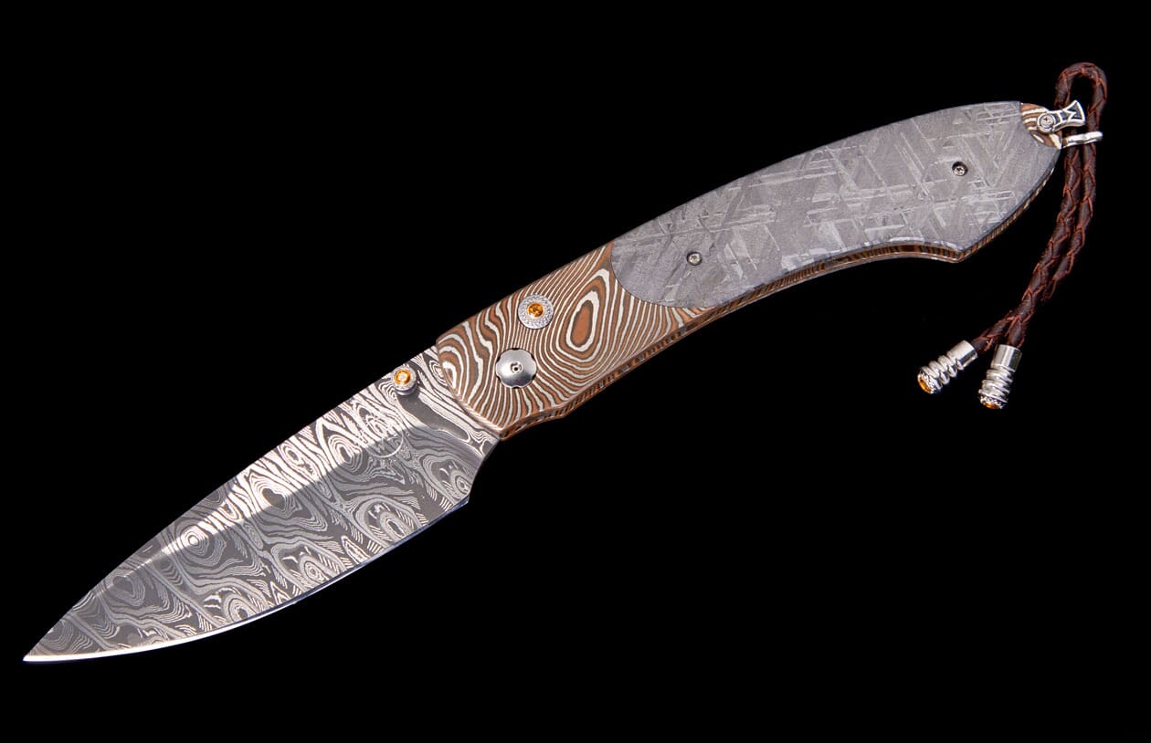 Damascus folding knife by Carefree Buffalo with patterned meteorite handle, gold accents, and braided leather lanyard.