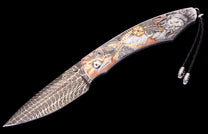 Custom folding knife with a Damascus steel blade and an engraved handle featuring a lion head, feathers, and a red gem accent, with a black leather lanyard.
