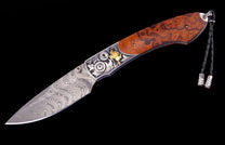 Ornate folding knife with a swirling Damascus steel blade, engraved silver bolster featuring a gold cowboy figure, burl wood handle, and black leather lanyard.