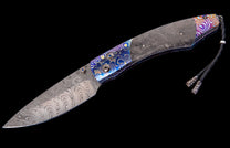 A folding knife with a swirling Damascus blade and a carbon fiber handle featuring vibrant, patterned metallic accents, and a braided leather lanyard.