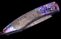 Folding knife with a dark marbled handle, iridescent purple and blue patterned bolsters, and a wavy Damascus steel blade.