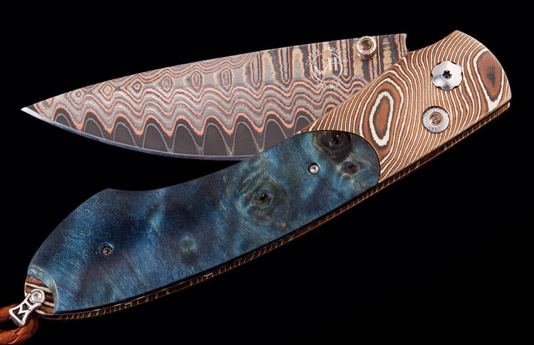 Folding knife with a wavy copper Damascus blade and a handle featuring blue burled wood and brown swirled material.