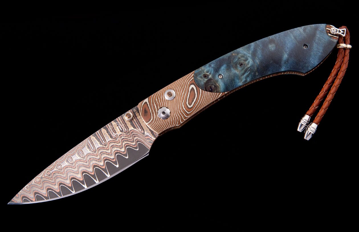 Damascus steel knife with a wavy-patterned blade, composite handle of patterned metal and blue burl wood, and a braided leather lanyard.