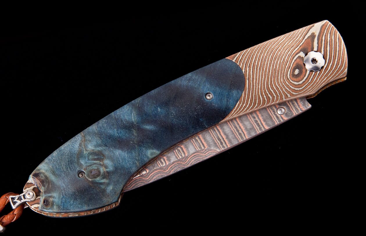 A folding knife with a dark blue swirling handle and Damascus steel featuring distinct brown and copper patterns.