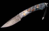 Decorative folding knife with a swirling Damascus blade, ornate silver bolsters featuring a white horse on gold, and a layered blue, orange, and white handle.