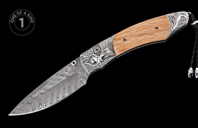 Open Damascus folding knife with wood handle, carved silver eagle bolsters, blue gems, and a braided black leather lanyard.