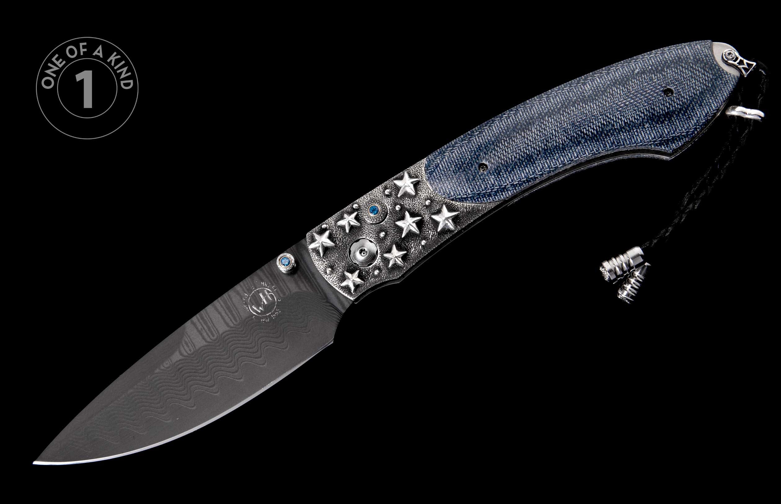 Folding knife with dark wavy Damascus blade, silver bolsters with stars and blue gems, a blue denim handle, and a decorative lanyard.