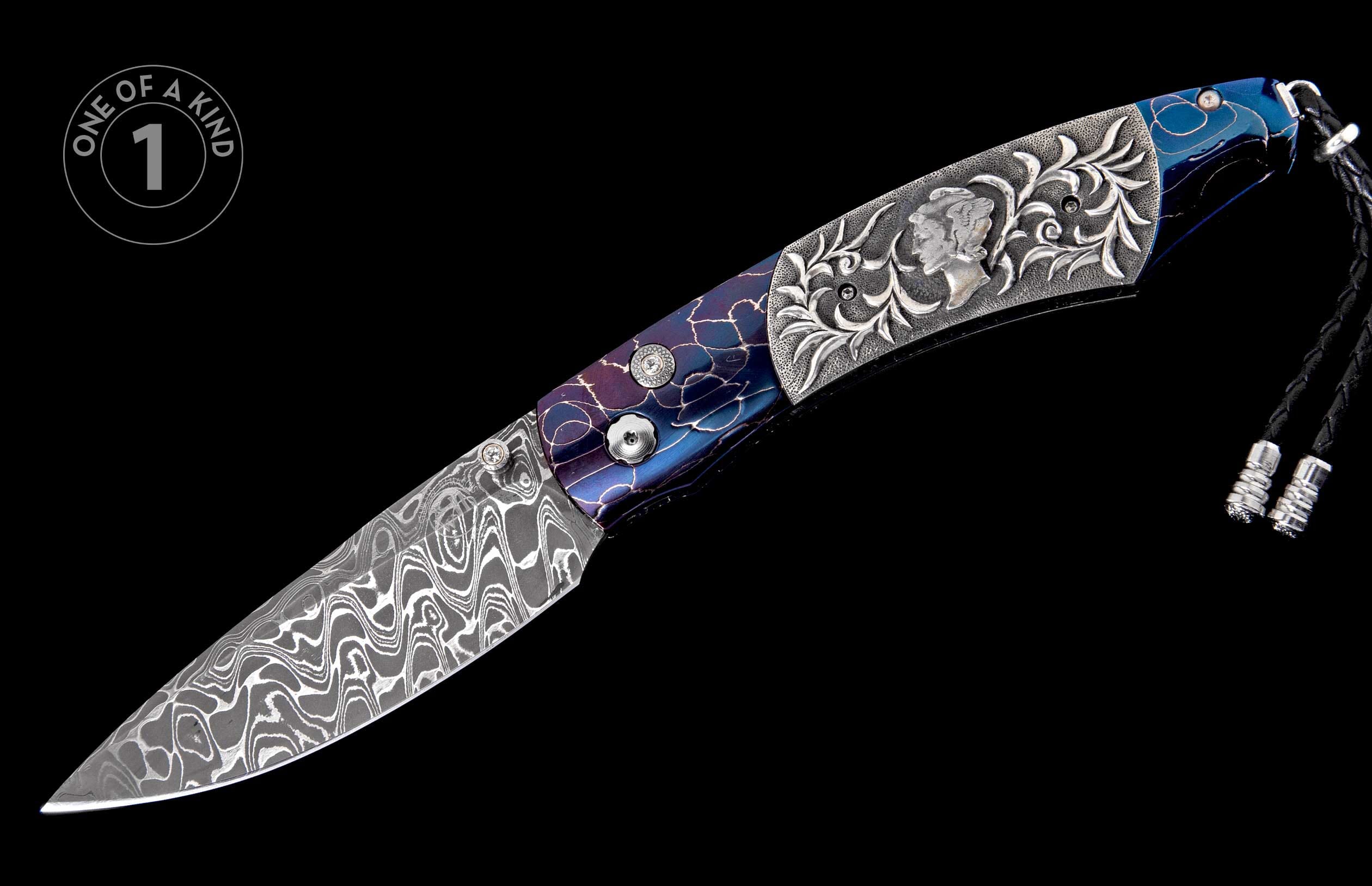 Damascus steel folding knife with a blue and purple patterned handle, ornate silver scrollwork, a carved bust, and a black leather lanyard.