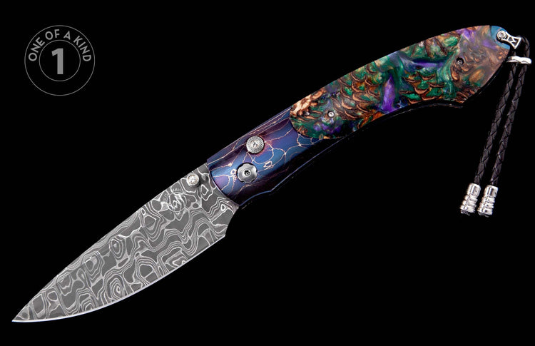 Ornate folding knife with a swirling Damascus steel blade and a multi-colored handle featuring abstract patterns, accented by a black braided lanyard.