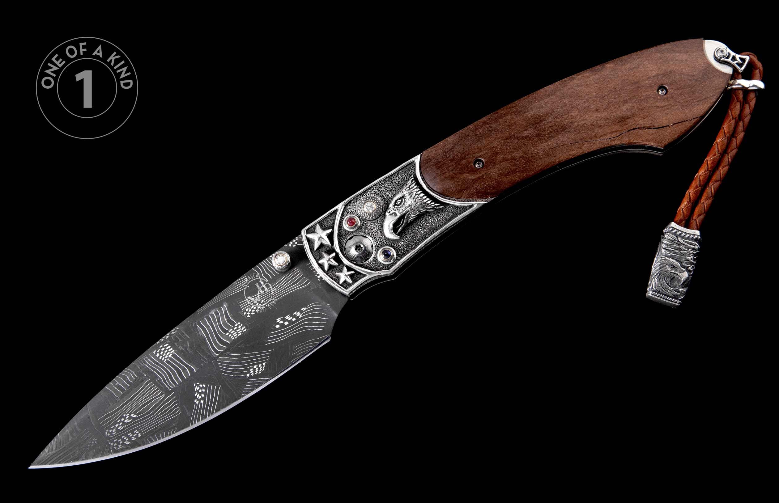 A decorative folding knife with a dark brown wooden handle, ornate silver-toned metal with an eagle head and gemstones, a Damascus steel blade, and a braided leather lanyard.