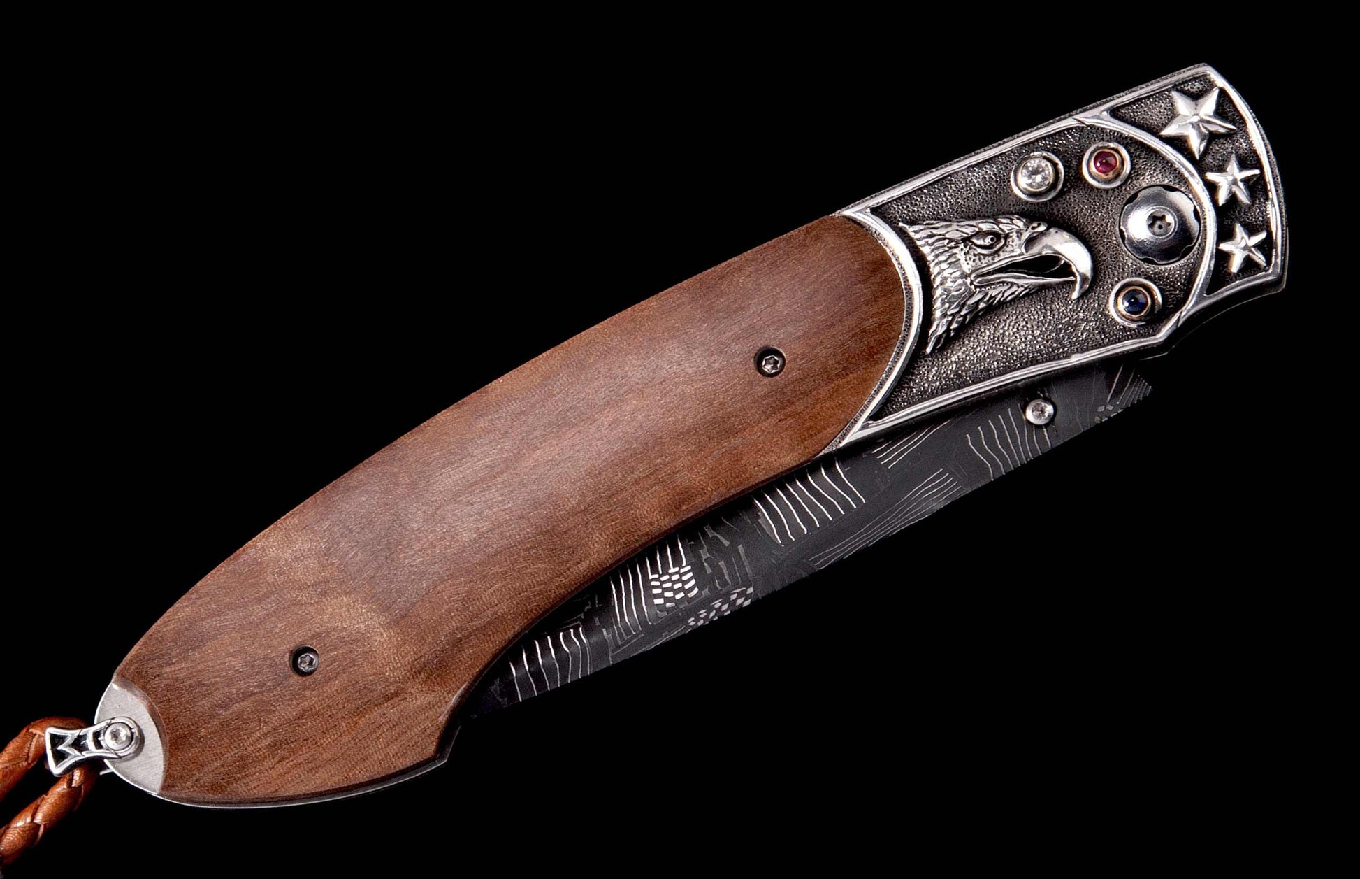 Folding knife with a brown wooden handle and a silver-toned bolster featuring an embossed eagle, stars, and colorful gems, partially revealing a patterned blade.