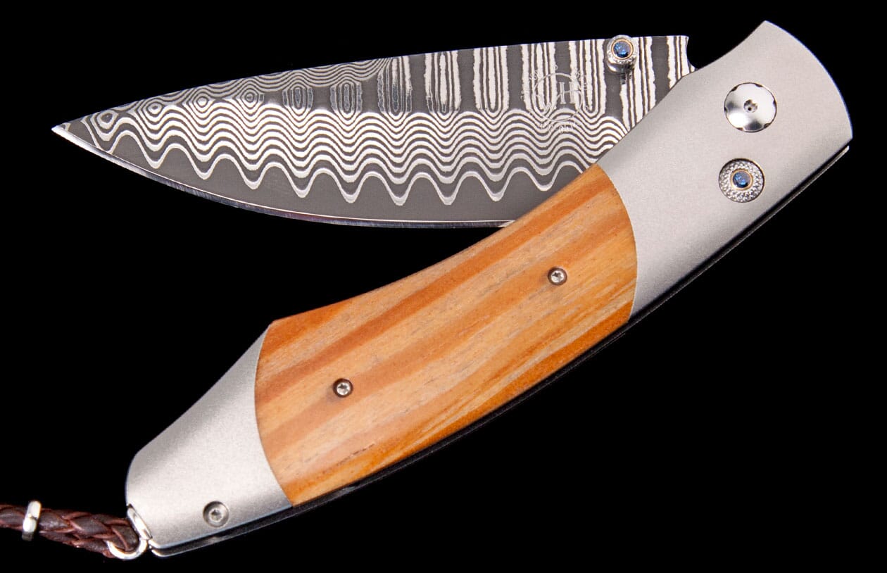 Folding knife with a wavy Damascus blade, light brown wood handle, and silver bolsters accented with blue details.