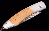 Folding knife with light wood handle, silver bolsters, and a patterned Damascus steel blade, with a braided leather lanyard.
