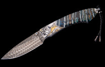 Custom knife with a patterned Damascus blade, gold marlin engraving, blue gemstone details, and a multi-striped handle with lanyard.