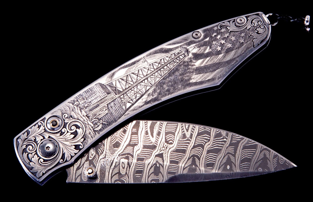Partially open silver-toned folding knife with engraved American flag and oil derrick handle, and a Damascus pattern blade.