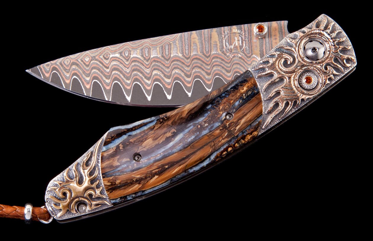 Custom folding knife with a wavy Damascus steel blade, a polished brown and blue handle, and ornate silver bolsters featuring bronze flame motifs and orange gemstones.