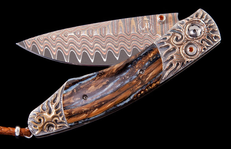 Custom folding knife with a wavy Damascus steel blade, a polished brown and blue handle, and ornate silver bolsters featuring bronze flame motifs and orange gemstones.