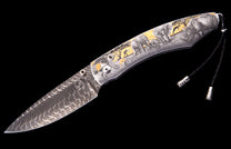 Folding knife with a patterned Damascus steel blade and a handle engraved with a gold-toned safari scene, plus a black leather lanyard.