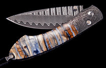 Custom folding knife by Tamreen, featuring a wavy Damascus blade and a striped handle of blue and brown fossilized mammoth tooth.