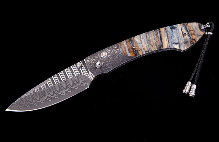 Damascus folding knife by Tamreen Custom, with a wavy patterned blade, intricate bolster, striped mammoth ivory handle, and leather lanyard.