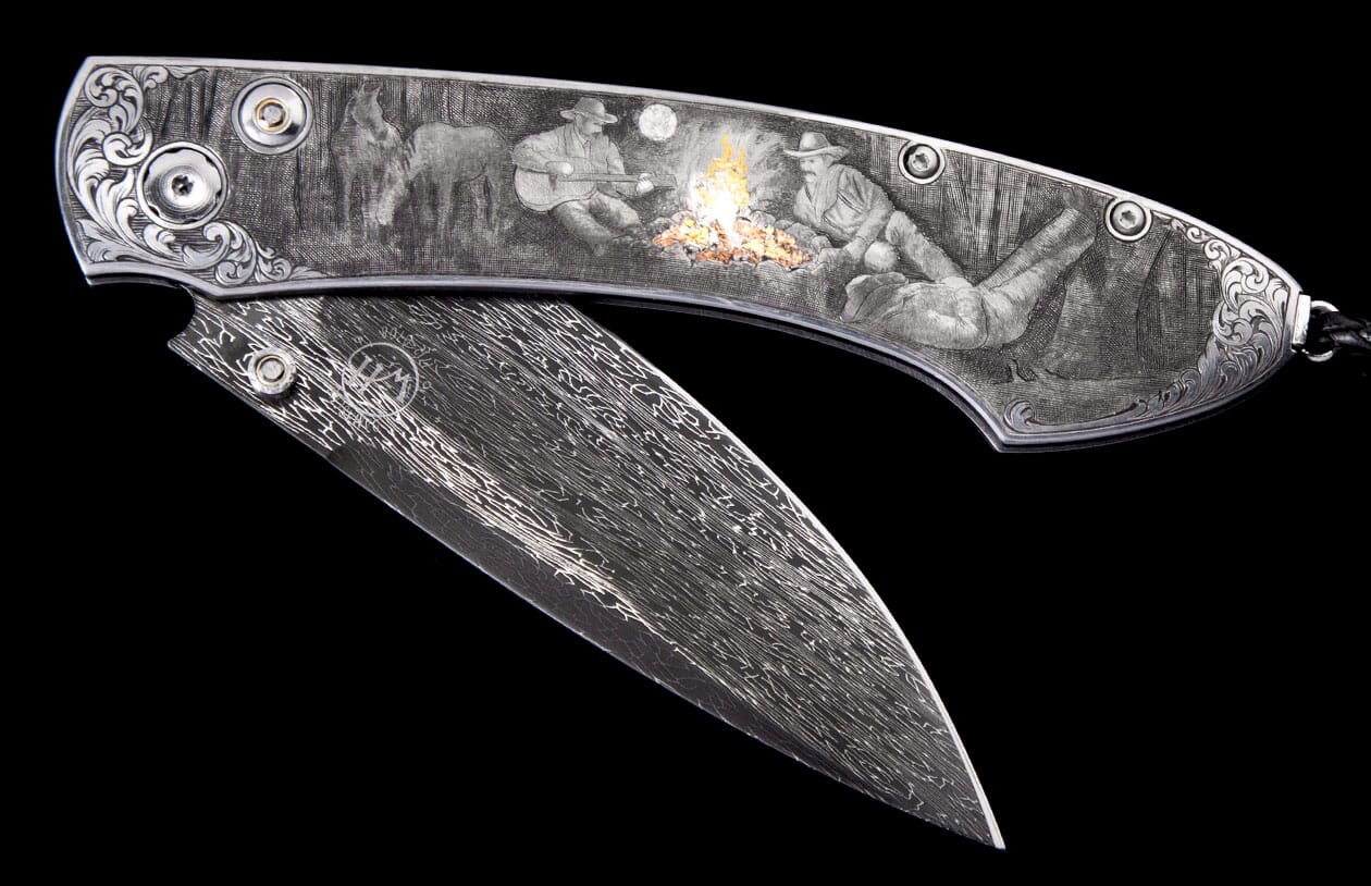 Engraved folding knife with Damascus steel blade, featuring a Western campfire scene of two men and a horse, partially open.