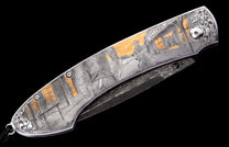 Silver-toned folding knife featuring an engraved Western scene of a cowboy and saloon with gold inlays, ornate scrollwork, and a dark Damascus-patterned blade.