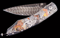 Silver-toned folding knife with a swirling Damascus blade and an engraved handle depicting a cowboy, horse, and saddle with gold and copper highlights.