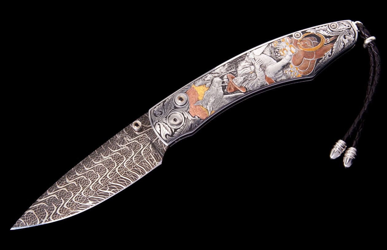 Western folding knife with Damascus blade, engraved handle showing silver, copper, and gold frontier scenes, and a leather lanyard.