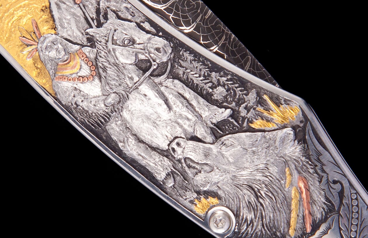 Western Frontier knife with intricate silver-toned engraving, featuring gold and copper accents of a rider and wolf, close-up.