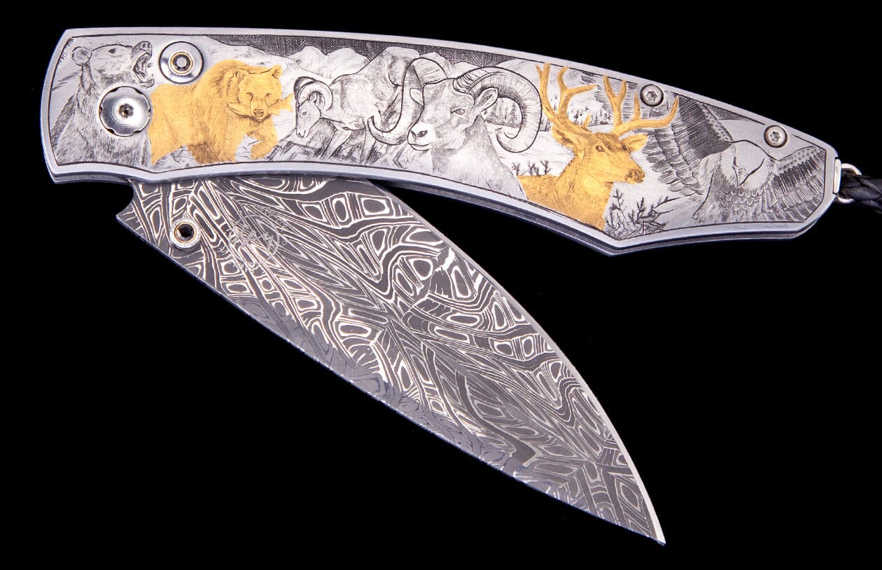 Open folding knife with a Damascus blade and engraved silver handle depicting a golden bear, rams, golden deer, and an eagle.