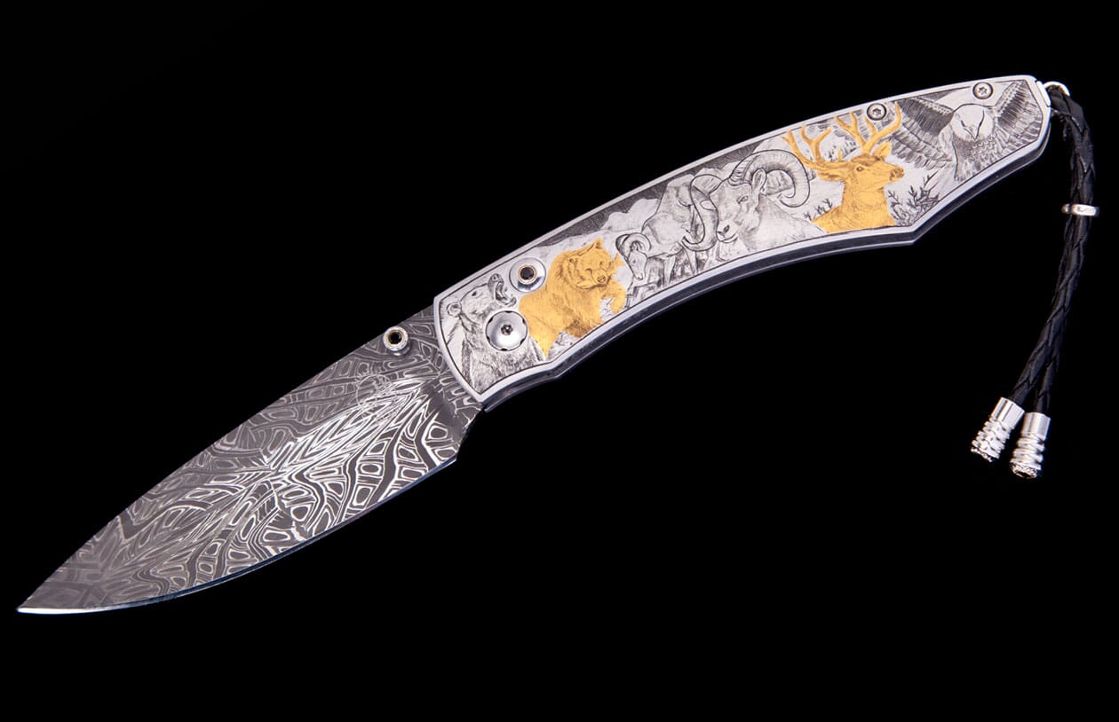 Damascus steel folding knife with an ornate handle featuring engraved wild animals, some in gold, and a braided leather lanyard.