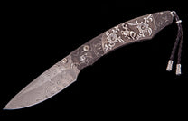 Damascus folding knife with an ornate handle featuring floral and cowboy engravings, and a braided leather lanyard.