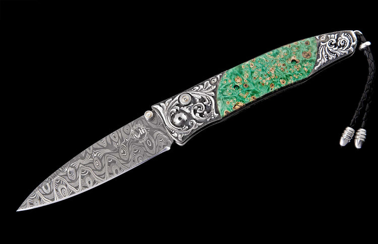 Ornate folding knife with a green burl handle, Damascus blade, intricately engraved silver frame, and a black leather lanyard.