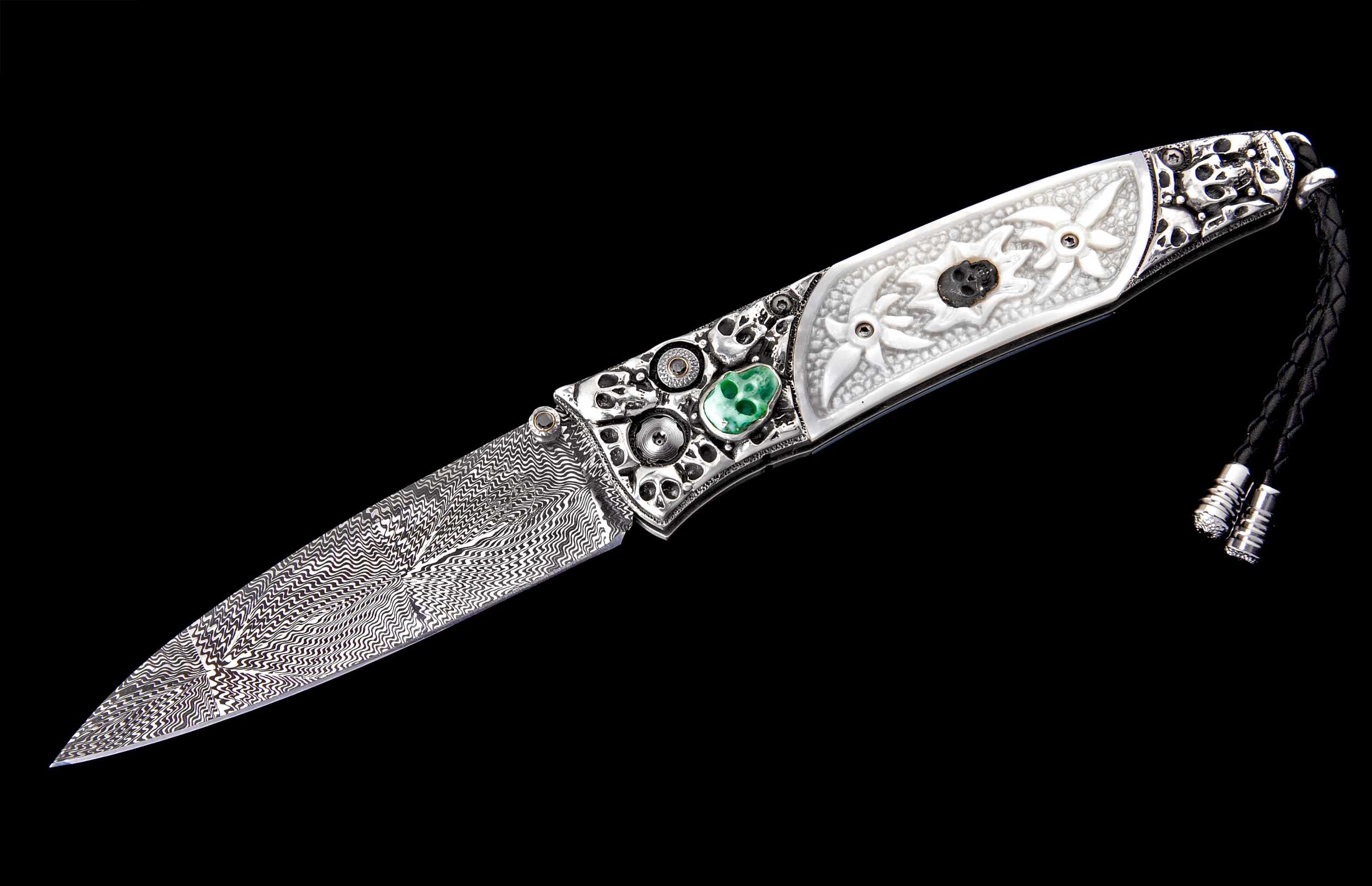 Ornate folding knife with a damascus blade, silver handle with carved skulls, white floral scales, and a green skull inlay.