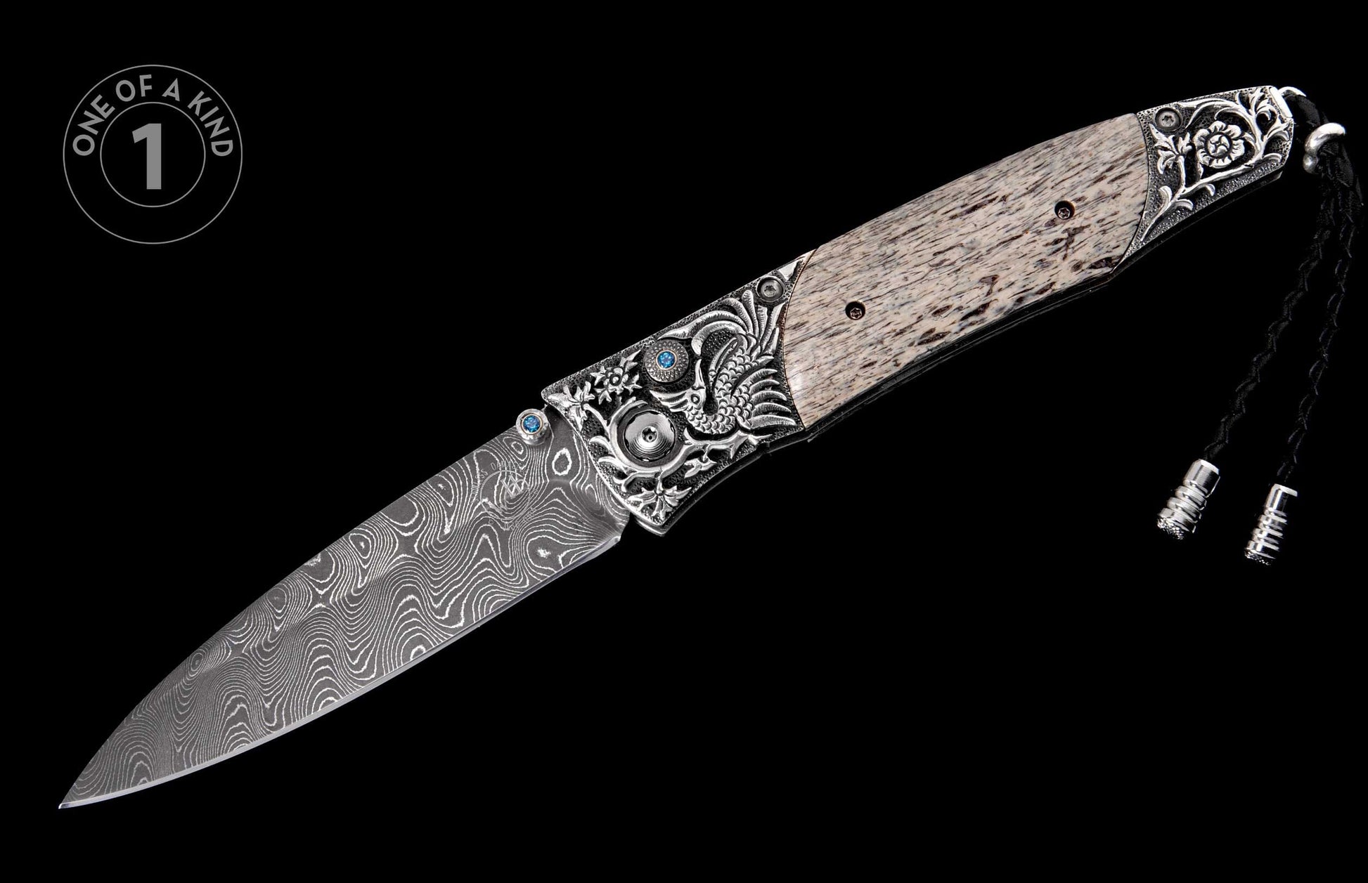 Folding knife with a wavy Damascus blade, ornate silver-tone bolsters with blue gemstones, a light patterned handle, and a black braided lanyard.