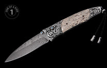 Folding knife with a wavy Damascus blade, ornate silver-tone bolsters with blue gemstones, a light patterned handle, and a black braided lanyard.