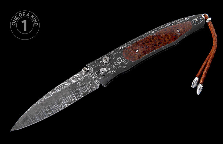 Open folding knife with patterned Damascus steel blade, patterned dark handle with textured red-brown inlay, and braided leather lanyard.