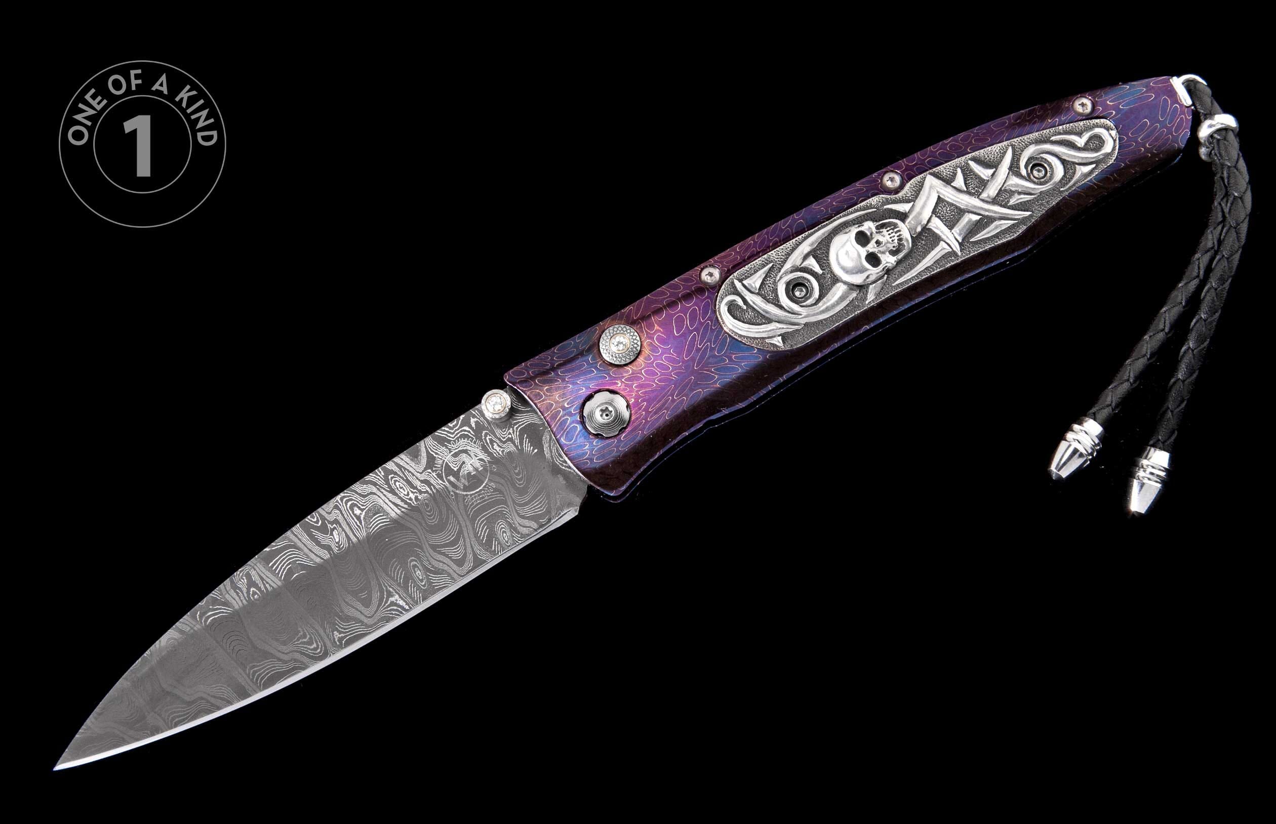 Open knife with a patterned Damascus blade, a purple iridescent handle featuring silver skull and scrollwork, and a black leather lanyard.