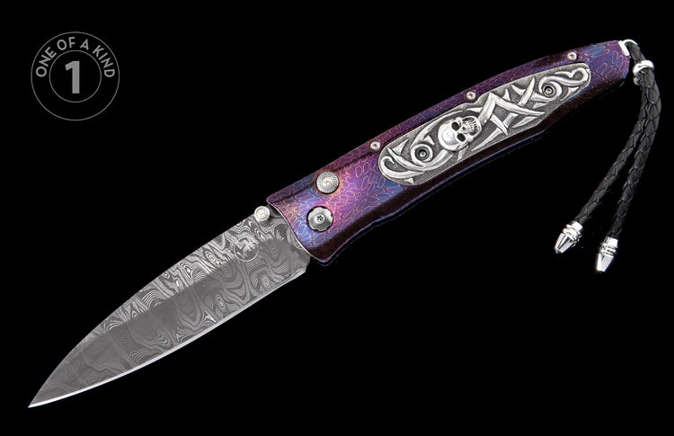 Open knife with a patterned Damascus blade, a purple iridescent handle featuring silver skull and scrollwork, and a black leather lanyard.