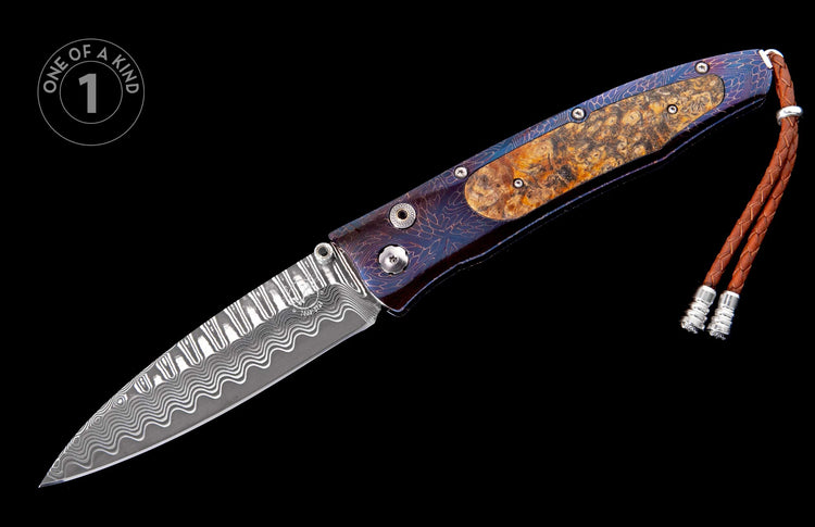 Damascus steel folding knife with a patterned handle, burl wood inlay, and a braided leather lanyard.